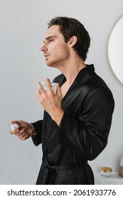 Young Man In Satin Robe Applying Perfume In Bathrobe