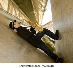 A Young Man With A Saxaphone Outdoors In An Industrial Setting.