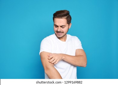 Young Man Scratching Arm On Color Background. Annoying Itch