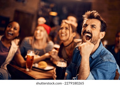 Young man screaming while watching sports game with his friends in a bar.