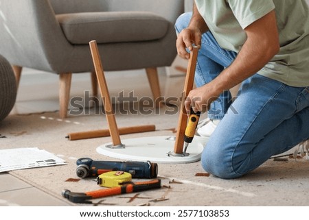 Young man with screwdriver assembling small table at home, closeup