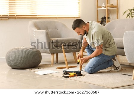 Young man with screwdriver assembling small table at home