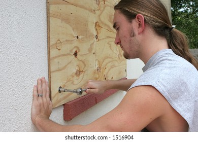 A Young Man Screwing Plywood Over A Window On His Home In Preparation For A Hurricane.