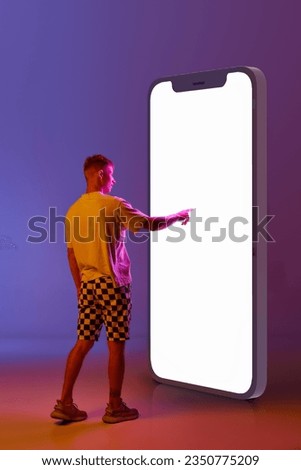 Young man scrolling giant 3d screen of mobile phone against gradient purple background in neon light. Concept of human emotions, youth, lifestyle, fashion, online shopping, sales, ad