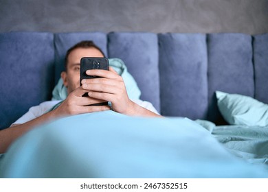 young man scrolls in smartphone in the morning after waking up, morning routine - Powered by Shutterstock