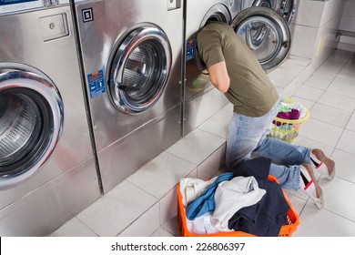 Young man searching clothes inside washing machine drum at laundromat