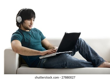 Young man seated on the couch working with a laptop and listen music at the same time