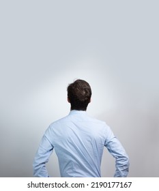 Young Man Seen From Behind Who Looks Up And Wonders. He Has His Hands On His Hips. Isolated On White Background With Free Place For Text.
