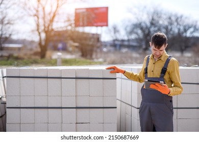 Young man seller shop assistant is verifying on a tablet an autoclaved aerated concrete block aac pallet on a construction shop store.