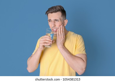 Young Man With Sensitive Teeth And Glass Of Cold Water On Color Background