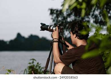 Young man setting up camera on the edge of the lake. Back view of man Setting up Camera with tripod