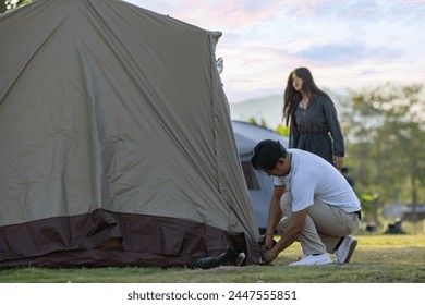 Young man setting up camp tent for camping trip on campground by hammering nail to the ground and Woman helps to set up a tent with cat playing near tent. - Powered by Shutterstock