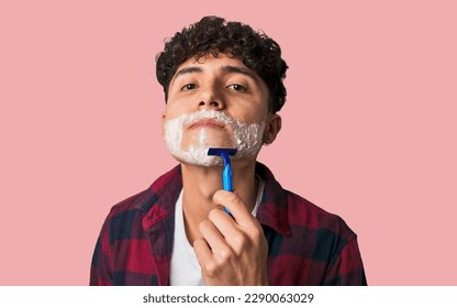 A young man shaves his beard with precision, using a razor blade and aftershave lotion for a clean, refreshing, and nourishing facial care routine. - Powered by Shutterstock