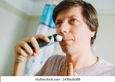 Young man shaving his face using an electric razor  in the bathroom - Shutterstock ID 1438636388