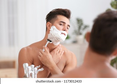 Young Man Shaving Near Mirror In Bathroom