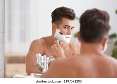 Young Man Shaving Near Mirror In Bathroom