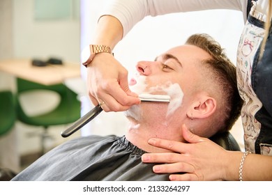 Young Man Shaving With Straight Edge Razor By Hairdresser In Barbershop