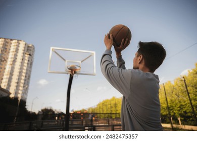 young man shoots a basketball at an outdoor hoop in the summer daytime - Powered by Shutterstock