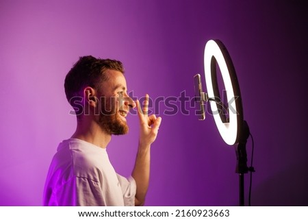 young man shoots a video on a phone with a ring lamp, portrait in color light