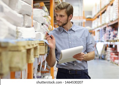 Young Man Shopping Or Working In A Hardware Warehouse Standing Checking Supplies On His Tablet.