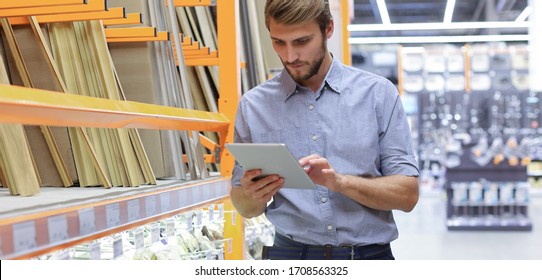 Young man shopping or working in a hardware warehouse standing checking supplies on his tablet. - Shutterstock ID 1708563325