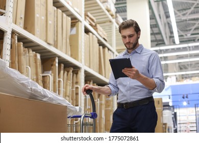 Young Man Shopping Or Working In A Hardware Warehouse Standing Checking Supplies On His Tablet.