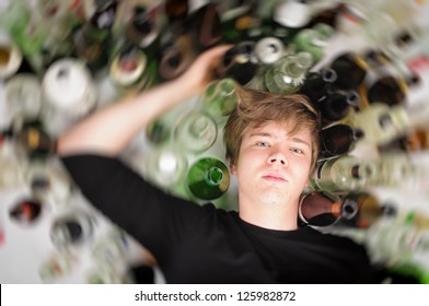 Young man with short blond hair lying on the floor and is surrounded by many empty beer and liquor bottles, upper perspective.