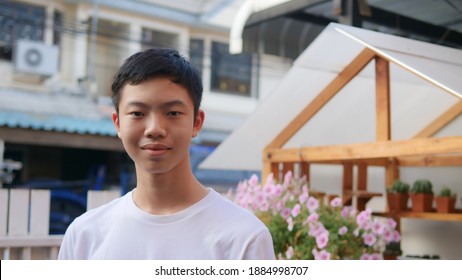 A Young Man With Short Hair, Black Hair, Handsome Face, Asian People, Thailand, Standing, Smiling, Happy Face. A Man Wearing A White T-shirt Stands In Front Of The House. Ornamental Trees. Healthy Por