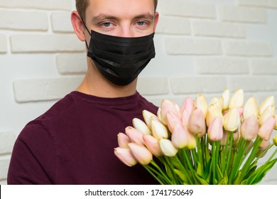 Young Man With Short Hair In A Medical Black Mask From The Period Of The Coronavirus Pandemic. Concept: Contactless Flower Delivery Service, Thanks To Doctors Who Work In Hospitals