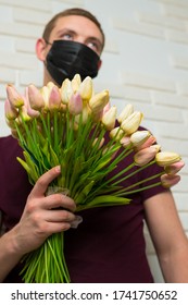 Young Man With Short Hair In A Medical Black Mask From The Period Of The Coronavirus Pandemic. Concept: Contactless Flower Delivery Service, Thanks To Doctors Who Work In Hospitals