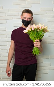 Young Man With Short Hair In A Medical Black Mask From The Period Of The Coronavirus Pandemic. Concept: Contactless Flower Delivery Service, Thanks To Doctors Who Work In Hospitals