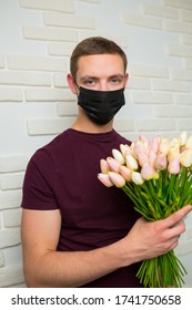 Young Man With Short Hair In A Medical Black Mask From The Period Of The Coronavirus Pandemic. Concept: Contactless Flower Delivery Service, Thanks To Doctors Who Work In Hospitals