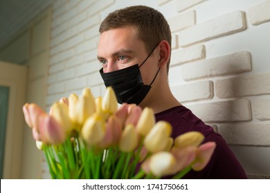 Young Man With Short Hair In A Medical Black Mask From The Period Of The Coronavirus Pandemic. Concept: Contactless Flower Delivery Service, Thanks To Doctors Who Work In Hospitals