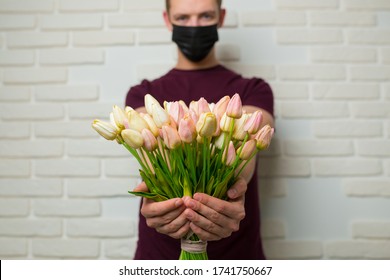 Young Man With Short Hair In A Medical Black Mask From The Period Of The Coronavirus Pandemic. Concept: Contactless Flower Delivery Service, Thanks To Doctors Who Work In Hospitals