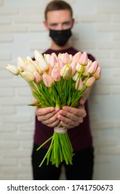 Young Man With Short Hair In A Medical Black Mask From The Period Of The Coronavirus Pandemic. Concept: Contactless Flower Delivery Service, Thanks To Doctors Who Work In Hospitals