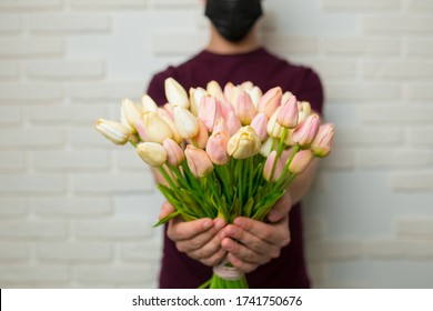 Young Man With Short Hair In A Medical Black Mask From The Period Of The Coronavirus Pandemic. Concept: Contactless Flower Delivery Service, Thanks To Doctors Who Work In Hospitals