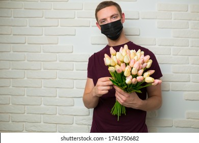 Young Man With Short Hair In A Medical Black Mask From The Period Of The Coronavirus Pandemic. Concept: Contactless Flower Delivery Service, Thanks To Doctors Who Work In Hospitals