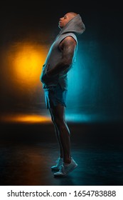 Young man in shorts and vest standing on tips of his toes. Colorful light on the background