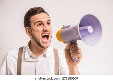 Young man is shouting in a megaphone over grey background. - Shutterstock ID 272680109