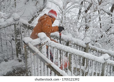 Young Man Shovelling Snow On Deck Staircase In Winter