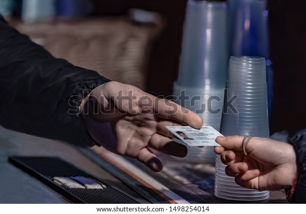 Young man show valid ID to\
buy alcohol and cigarettes in pub photographed with shallow depth\
of field