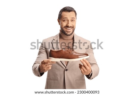 Young man showing a brown leather shoe and smiling isolated on white background