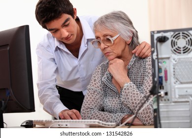 Young Man Showing Elderly Lady How To Use Computer