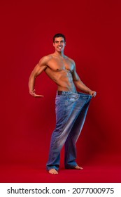Young man showing how much weight he lost with big jeans. Fat to fit concept. Fitness poster on red background