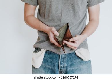 Young man shows his empty leather wallet. Concept of unemployed and having bankruptcy no money, isolated on white background.