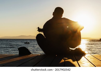 young man in silhouettes playing guitar at sunset beach