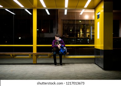 Young Man Sit On The Bus Stop Bench Waiting In The Night