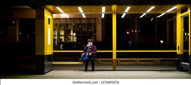 Young Man Sit On The Bus Stop Bench Waiting In The Night