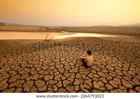 Young man sit on dry cracked earth near drying river or lake metaphor Water crisis, Drought and climate change.