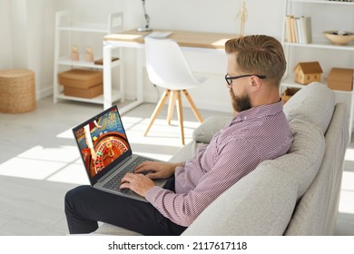 Young man sit relax on sofa play casino online on computer. Caucasian male rest at home couch gamble internet on laptop. Entertainment on web. Gambler or gamer Russian roulette. - Shutterstock ID 2117617118